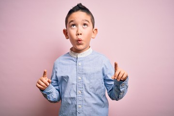 Young little boy kid wearing elegant shirt standing over pink isolated background amazed and surprised looking up and pointing with fingers and raised arms.