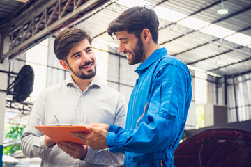 Obraz premium Mechanic holding clipboard with car owner in the workshop garage. Car auto services concepts