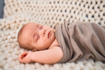 Adorable baby lying down on the sofa over blanket at home. Newborn relaxing and sleeping comfortable