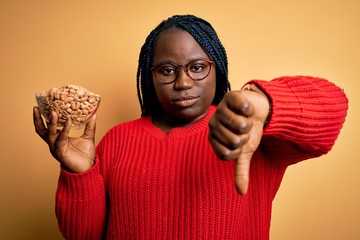 Young african american plus size woman with braids holding bowl with healthy peanuts with angry...