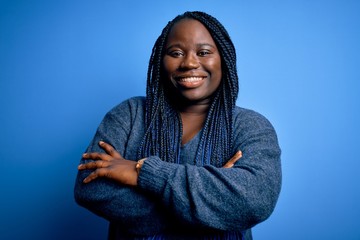 African american plus size woman with braids wearing casual sweater over blue background happy face...