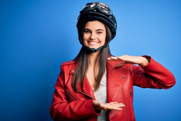 Fototapeta na wymiar Young beautiful brunette motorcycliste woman wearing motorcycle helmet and jacket gesturing with hands showing big and large size sign, measure symbol. Smiling looking at the camera. Measuring