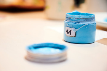 Kleine Dose gefüllt mit hellblauer Farbe und beklebt mit der Zahl 11 steht auf einem hellen Tisch.
