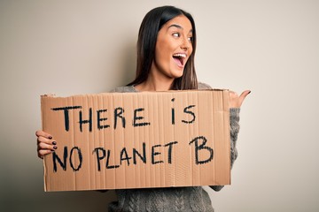Young beautiful brunette activist woman protesting for save the planet holding banner pointing and...