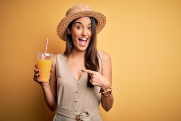 Young beautiful woman on vacation wearing summer hat drinking healthy orange juice very happy...