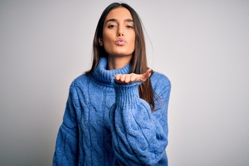 Young beautiful brunette woman wearing casual turtleneck sweater over white background looking at the camera blowing a kiss with hand on air being lovely and sexy. Love expression.