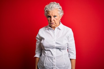 Senior beautiful woman wearing elegant shirt standing over isolated red background skeptic and nervous, frowning upset because of problem. Negative person.