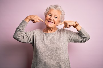 Senior beautiful woman wearing casual t-shirt standing over isolated pink background smiling cheerful showing and pointing with fingers teeth and mouth. Dental health concept.