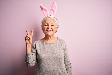 Senior beautiful woman wearing bunny ears standing over isolated pink background smiling with happy...