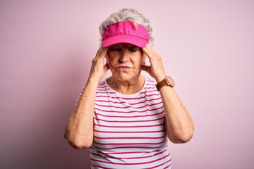 Senior beautiful sporty woman wearing sport cap standing over isolated pink background suffering from headache desperate and stressed because pain and migraine. Hands on head.