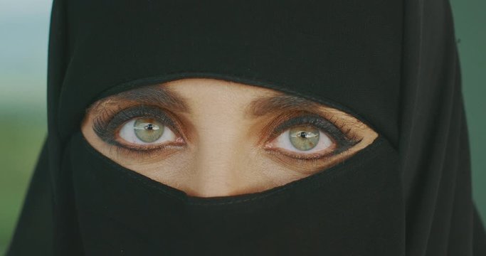 Portrait of a muslim woman wearing traditional black niqab showing only her green eyes, middle east culture