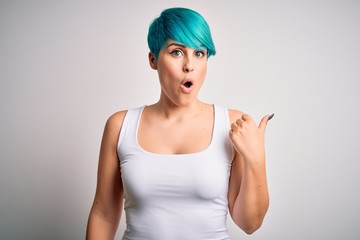 Young beautiful woman with blue fashion hair wearing casual t-shirt over white background Surprised pointing with hand finger to the side, open mouth amazed expression.