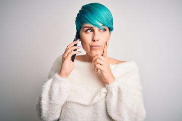 Young woman with blue fashion hair having a conversation talking on smartphone serious face thinking about question, very confused idea