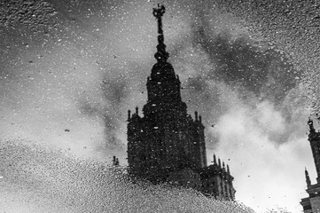 Reflection of a part of a building. Moscow State University. A puddle on the pavement. Black and white photography.