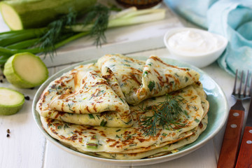 Snack or summer lunch. Zucchini pancakes with greens served with sour cream on a wooden table.