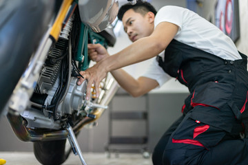 Naklejka na ściany i meble Asian mechanic man fixing the retro motorcycle in the garage