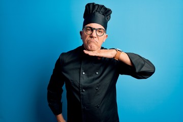 Middle age handsome grey-haired chef man wearing cooker uniform and hat cutting throat with hand as knife, threaten aggression with furious violence