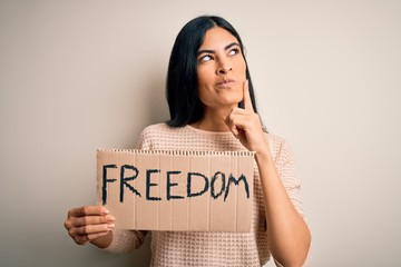 Young beautiful hispanic woman holding protest banner of freedom asking for liberty serious face...