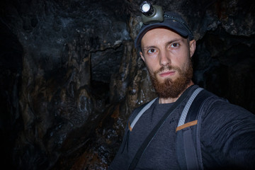 Fototapeta na wymiar Bread man in the cave make selfie dressed in hat and shirt with bag and flashlight