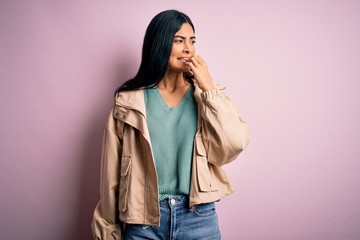 Young beautiful hispanic fashion woman wearing winter jacket and sweater over pink background...