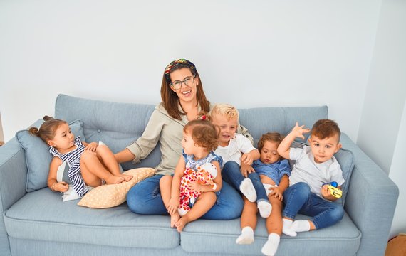 Beautiful teacher and group of toddlers sitting on the sofa playing at kindergarten