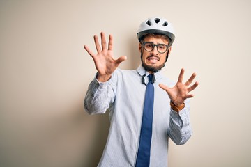 Young businessman wearing glasses and bike helmet standing over isolated white bakground afraid and terrified with fear expression stop gesture with hands, shouting in shock. Panic concept.