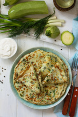 Snack or summer lunch. Zucchini pancakes with greens served with sour cream on a wooden table. Top view flat lay background.