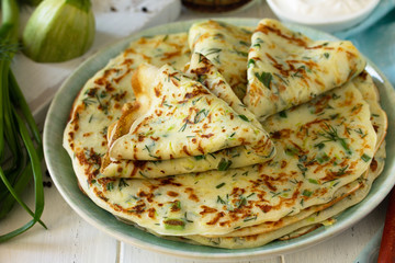 Summer lunch or Snack. Zucchini pancakes with greens served with sour cream on a wooden table.