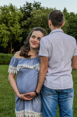 Obraz premium Young couple in love on a walk in the park, husband hugs pregnant wife by the belly, happy family