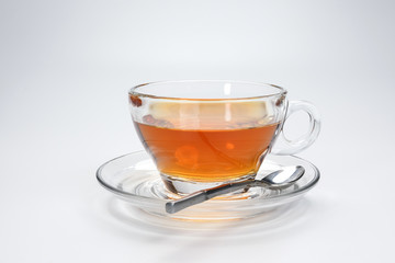 Clear licker tea in a transparent glass cup saucer spoon on white background