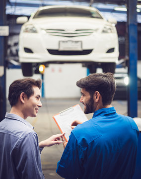 Mechanic Holding Clipboard With Car Owner In The Workshop Garage. Car Auto Services Concepts