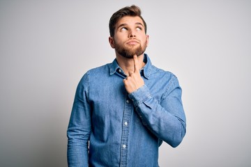 Young handsome blond man with beard and blue eyes wearing casual denim shirt Thinking concentrated about doubt with finger on chin and looking up wondering