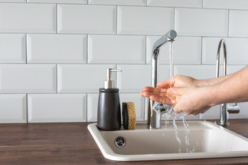 Hand washing underwater from a faucet in the kitchen. leanliness, water saving, washing dishes in a bright Scandinavian interior