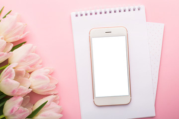 Mobile phone, notebook and spring flower pink tulips on the pink background. Theme of love, mother's day, women's day flat lay
