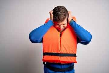 Young blond tourist man with beard and blue eyes wearing lifejacket over white background suffering...