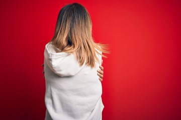 Middle age beautiful sportswoman wearing casual sweatshirt over isolated red background Hugging...