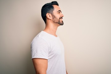 Young handsome man with beard wearing casual t-shirt standing over white background looking to...