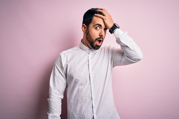 Fototapeta premium Young handsome man with beard wearing casual shirt standing over pink background surprised with hand on head for mistake, remember error. Forgot, bad memory concept.