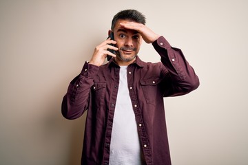 Young handsome man having conversation talking on the smartphone over white background stressed with hand on head, shocked with shame and surprise face, angry and frustrated. Fear and upset