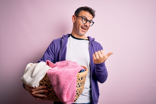 Young handsome man doing housework holding wicker basket with clothes pointing and showing with thumb up to the side with happy face smiling