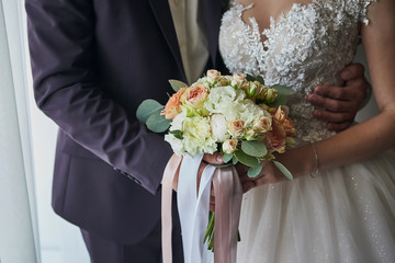 Bride holding a wedding bouquet in the hands standing near groom