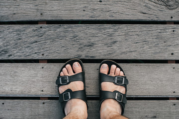 Top view shot of A traveler feet standing alone at the pathway of a wooden bridge.Pair of shoes in the middle, they are on the weathered wooden bridge and above the river. Concept Standing on the brid