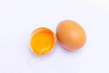 Two brown eggs With one egg broken in half, with a yolk inside the eggshell, laid on a white background