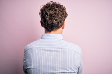 Young blond handsome man with curly hair wearing striped shirt over white background standing backwards looking away with crossed arms - Powered by Adobe