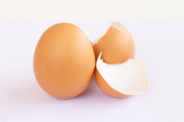 One brown egg laying on a broken eggshell on a white background.