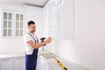 Worker installing handle on cabinet door with screw gun in kitchen