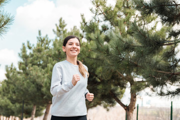 healthy lifestyle. cheerful attractive woman running in park with pine trees in the morning