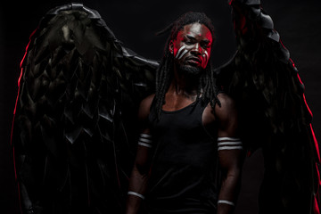 shirtless african man with naked torso in the flesh of black angel, african guy has muscular athletic body, wearing artificial black magnificent wings on back, posing at camera. isolated black