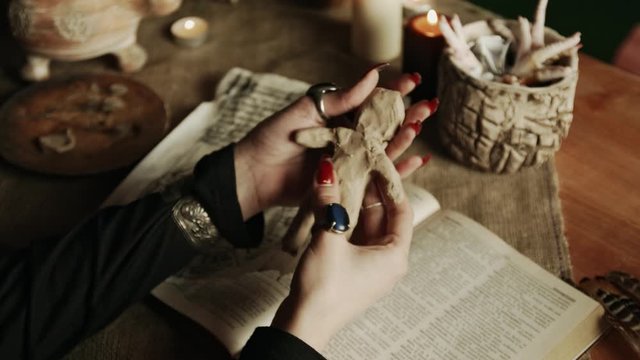Partial view of witch putting needles in voodoo doll near magic book