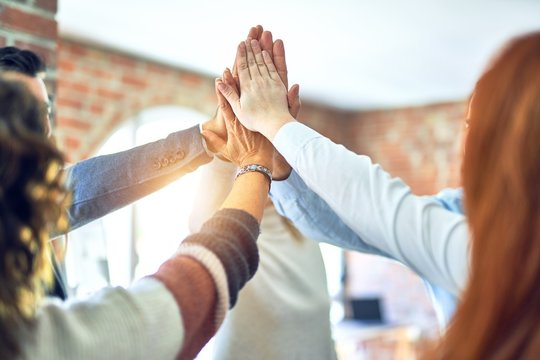 Group of business workers standing with hands together highing five at the office